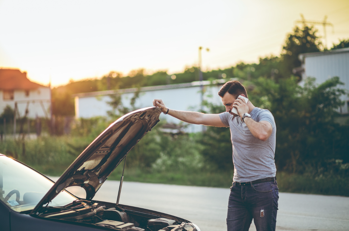 Male driver lifting car bonnet and talking on the phone to roadside assistance